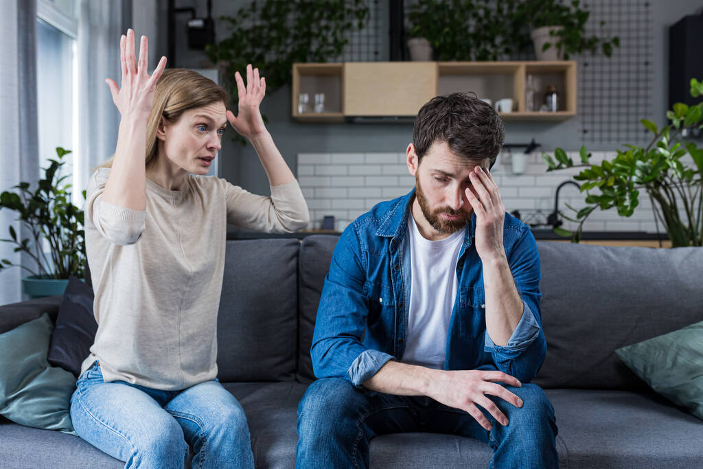 Family quarrel, man and woman sitting on sofa at home. angry woman yells at her husband, blames. The man is silent. He listens, holds his head, embarrassed - Photo, Image