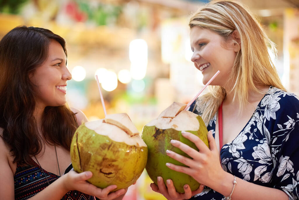 Razem na trzy. Ujęcie dwóch młodych kobiet pijących kokosy w obcym sklepie spożywczym.. - Zdjęcie, obraz