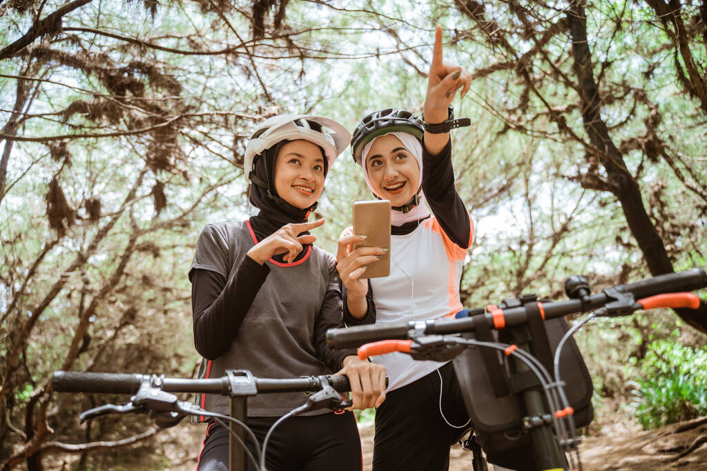 Kaksi naista pyöräilemässä matkapuhelimella osoittaa tietä - Valokuva, kuva
