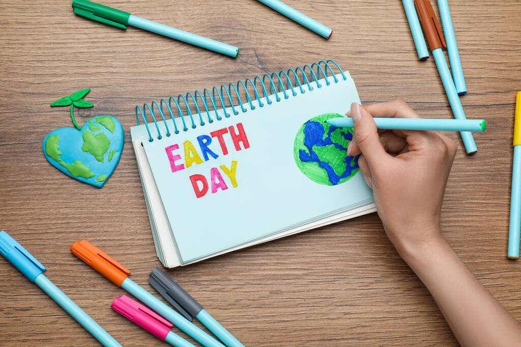 Happy Earth Day. Woman drawing planet in notebook at wooden table, top view - Photo, image