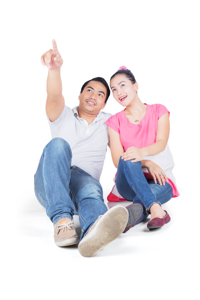 Young couple pointing something while sitting in the studio. Isolated on white background - Photo, Image