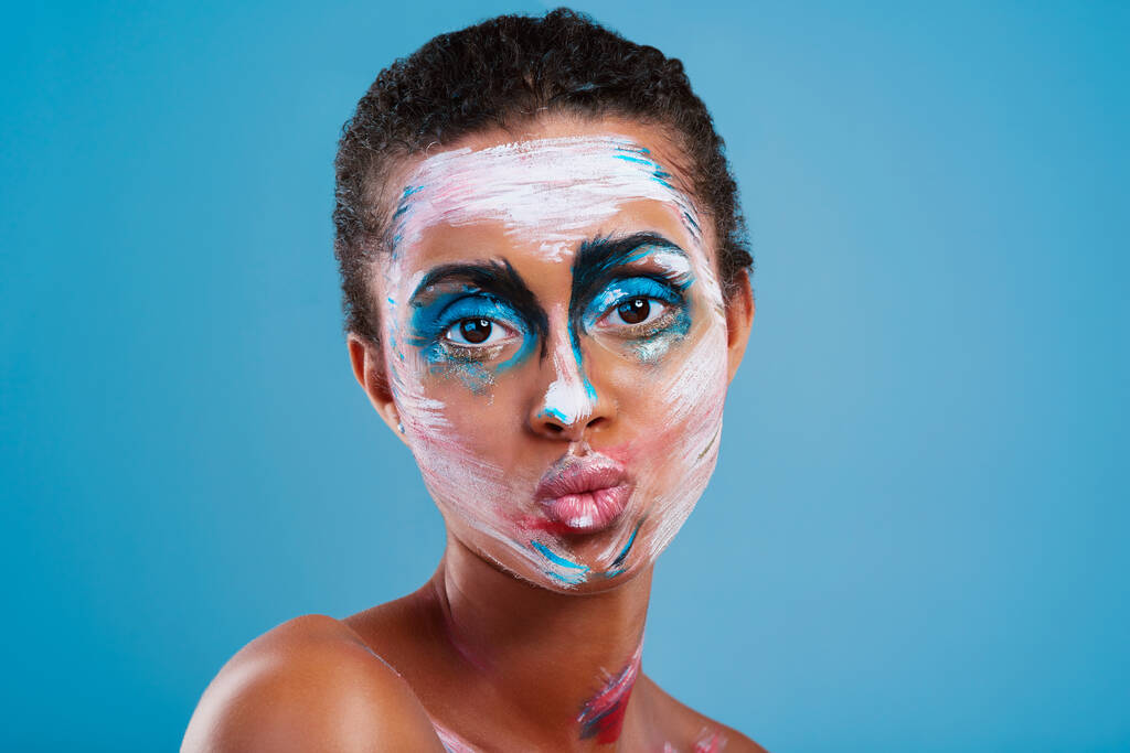 Meer dan alleen een mooi gezicht. Studio portret van een mooie jonge vrouw bedekt met gezicht verf poseren tegen een blauwe achtergrond. - Foto, afbeelding