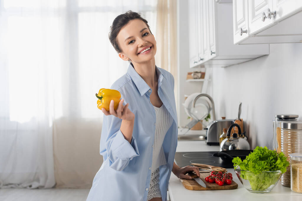 pleased woman holding bell pepper near cherry tomatoes and fresh lettuce - Foto, afbeelding