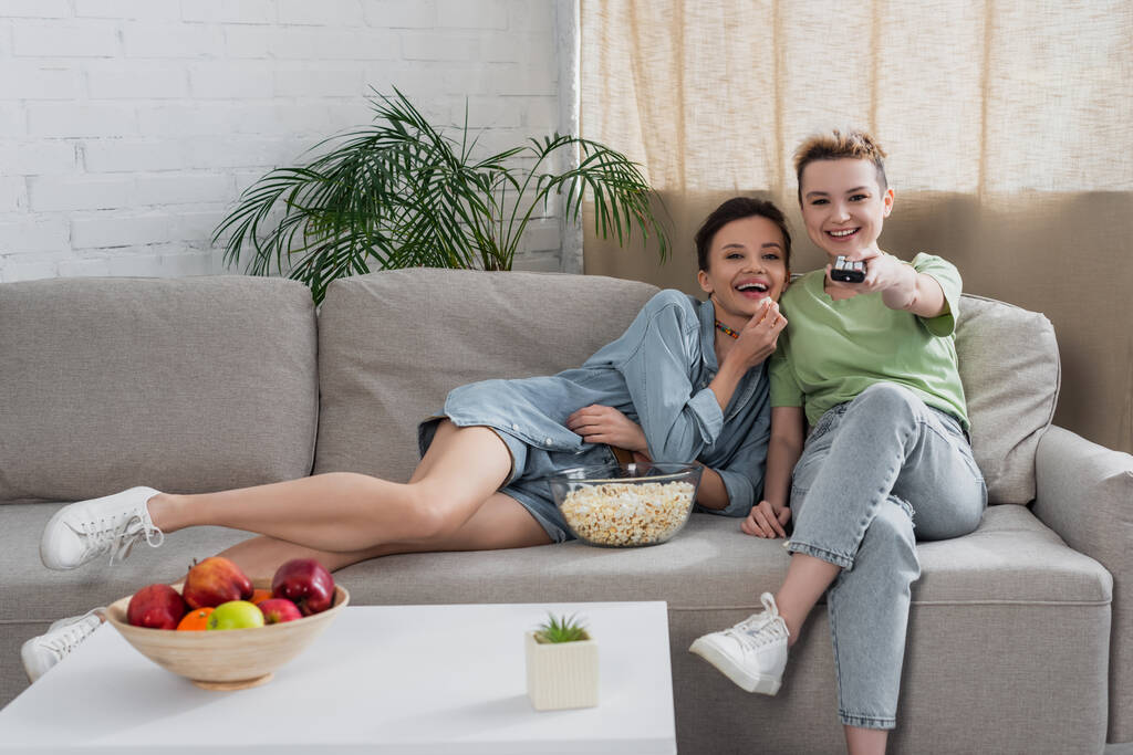 laughing pansexual couple watching movie on tv near popcorn and fresh apples - Foto, Imagem