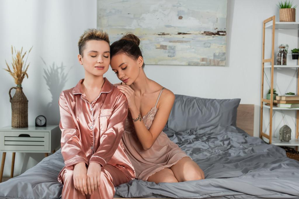 bigender person with closed eyes sitting on bed near young partner - Valokuva, kuva
