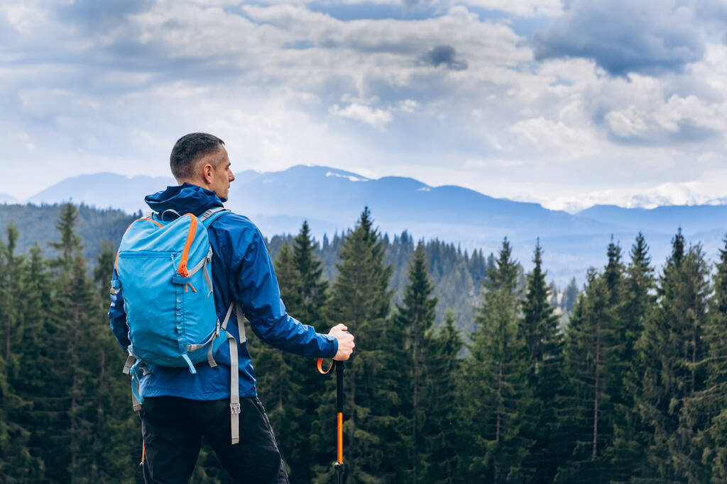 Homem desportivo com mochila a olhar para o vale da montanha. Paisagem com viajante, colinas nebulosas, floresta, céu nublado - Foto, Imagem