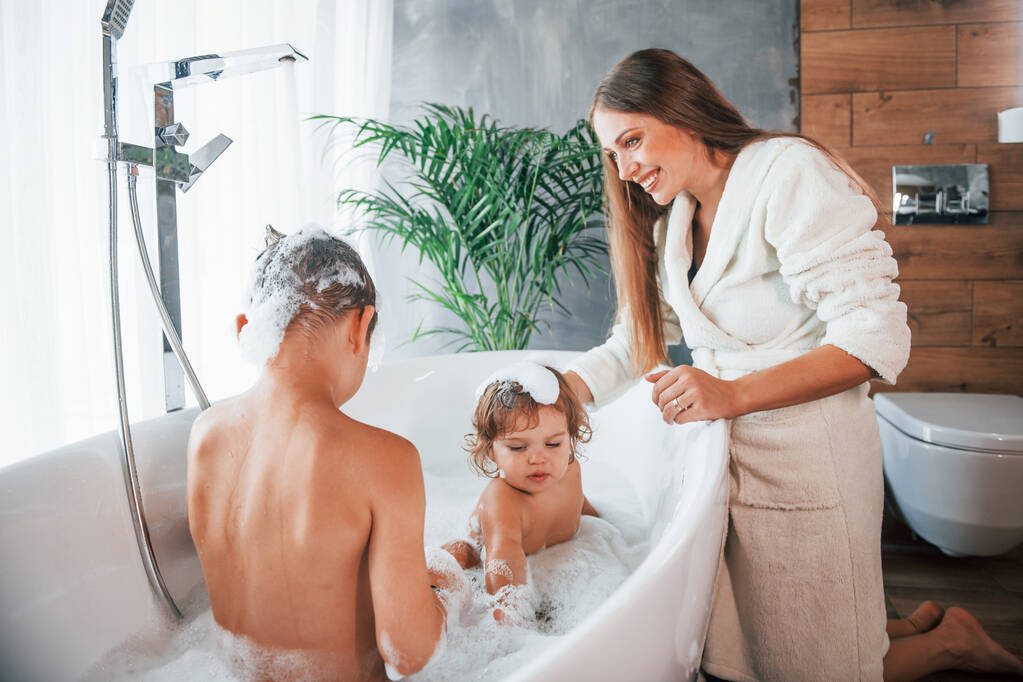 Having fun. Young mother helps her son and daughter. Two kids washing in the bath. - Foto, imagen