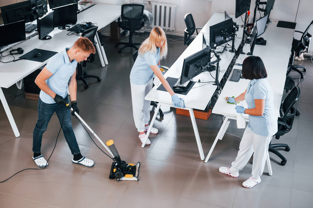 Limpia el suelo. Grupo de trabajadores limpian oficina moderna juntos durante el día. - Foto, Imagen