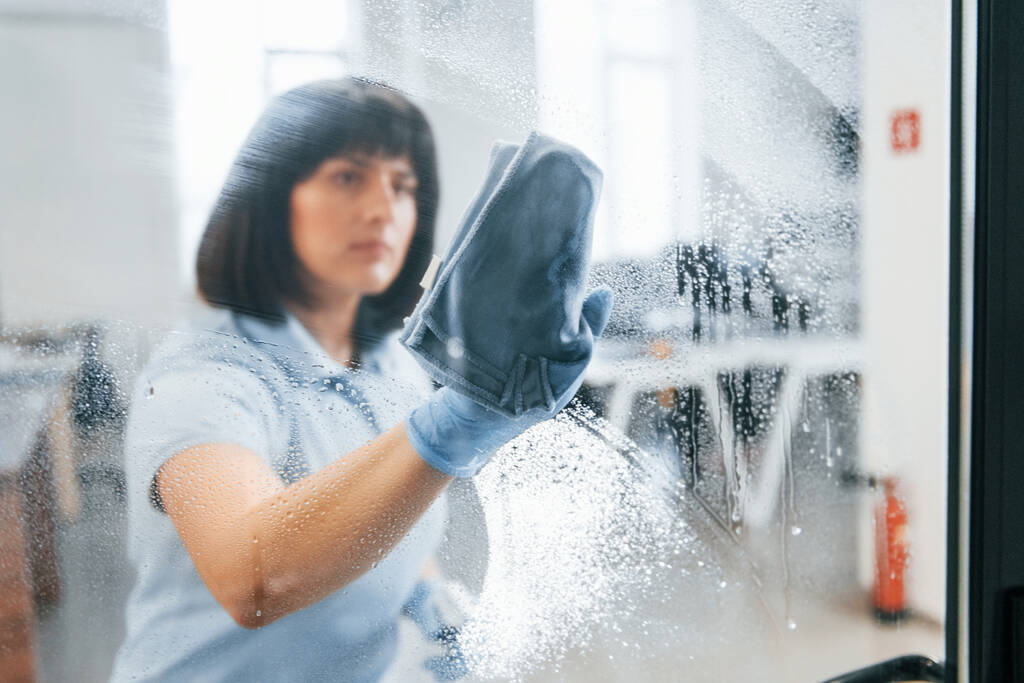 Женщина моет грязное окно полотенцем. Вид через стекло. - Фото, изображение