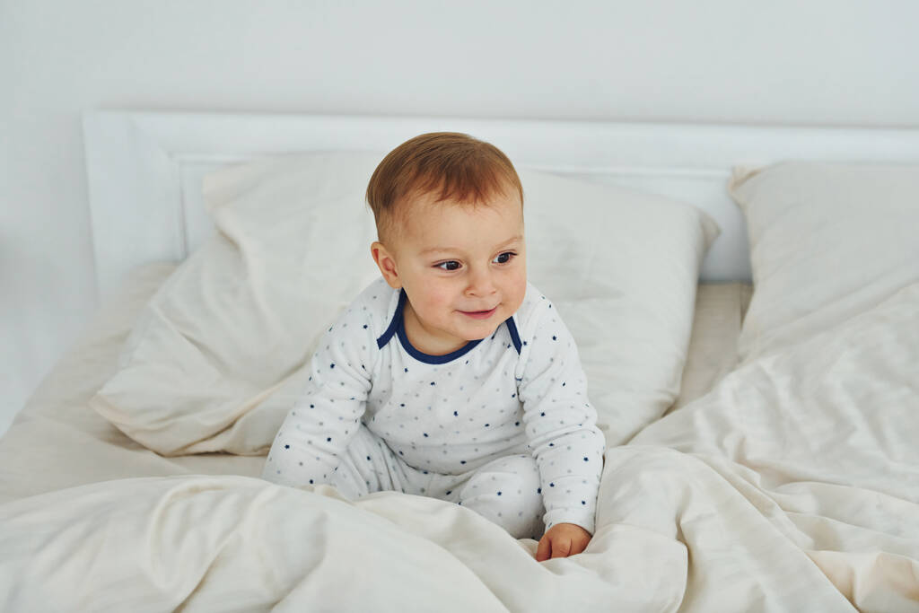 Aranyos kisfiú van az ágyon. Belső tér és design gyönyörű modern hálószoba nappal. - Fotó, kép