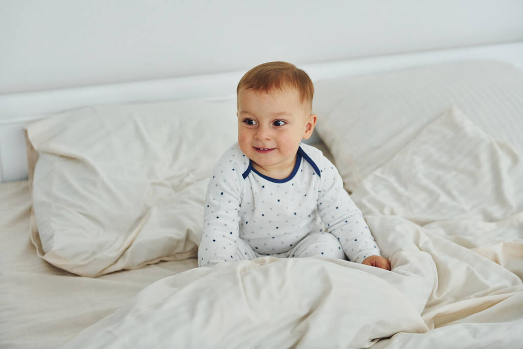 Aranyos kisfiú van az ágyon. Belső tér és design gyönyörű modern hálószoba nappal. - Fotó, kép