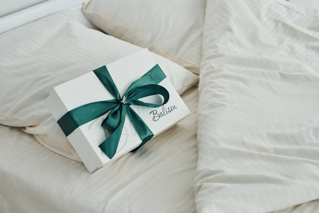 Gift box is on the white bed. Interior and design of beautiful modern bedroom at daytime. - Фото, изображение