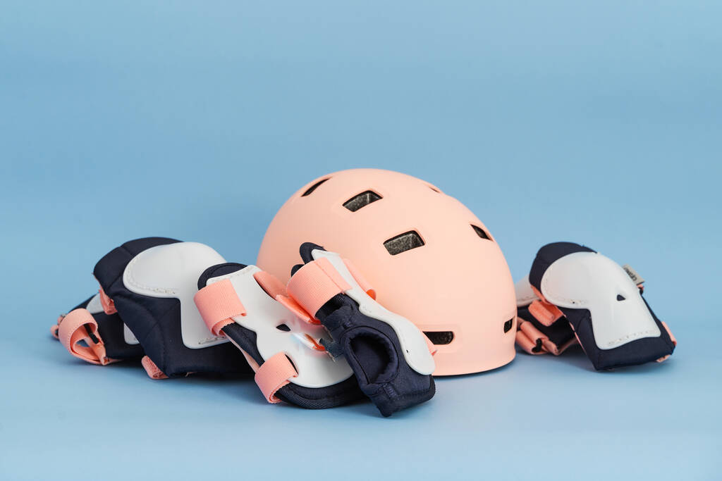 Top view of roller skates protective gear set - knee, elbow and wrist pads and helmet in pink colors. Blue background flat lay  - Zdjęcie, obraz