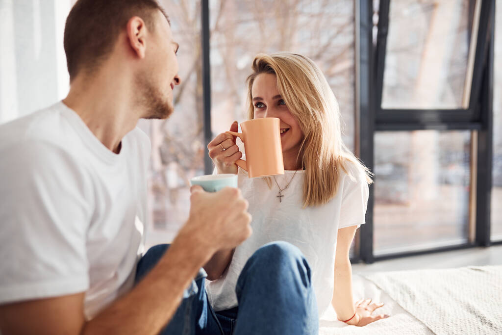 Νεαρό υπέροχο ζευγάρι μαζί πίνοντας ζεστό τσάι στο σπίτι περνούν το Σαββατοκύριακο και τις διακοπές μαζί. - Φωτογραφία, εικόνα