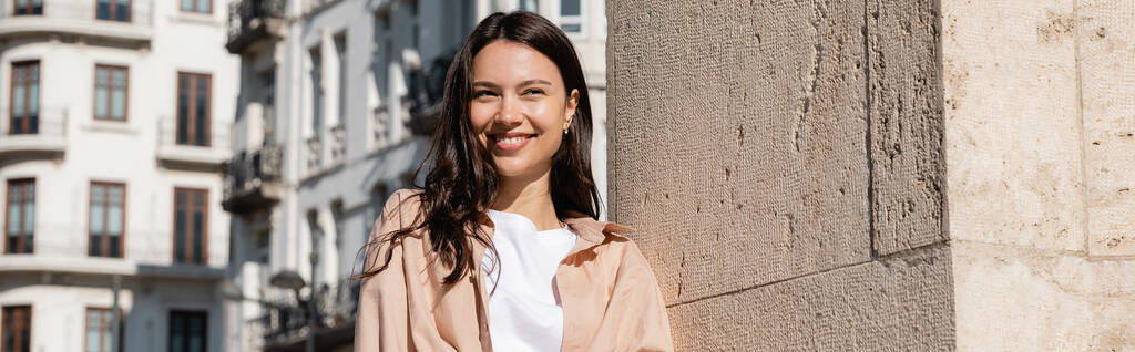 šťastná brunetka žena usmívající se na ulici v blízkosti zdi, prapor - Fotografie, Obrázek