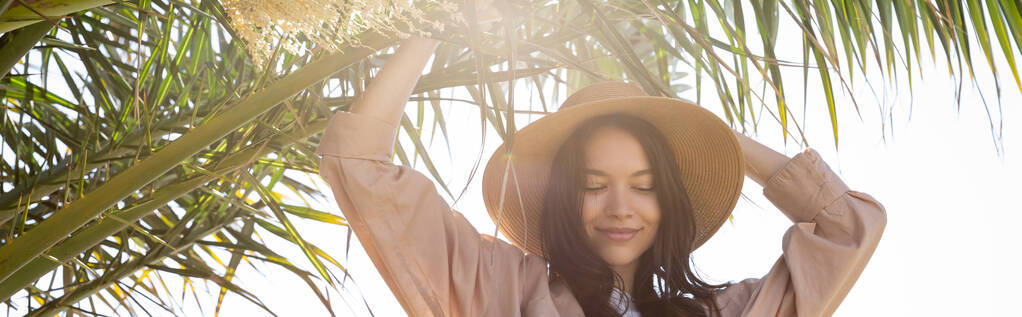 piacere bruna donna in cappello di paglia in piedi vicino alla palma verde, striscione - Foto, immagini