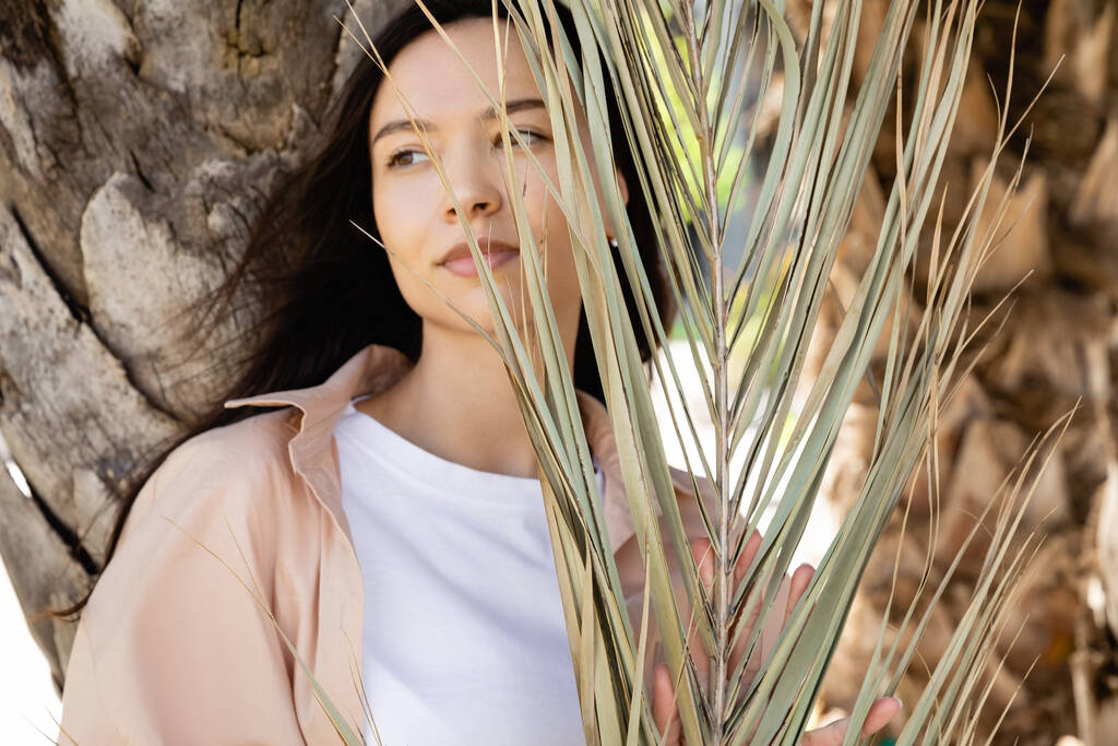 brunette woman looking away near dry palm leaves  - Photo, Image