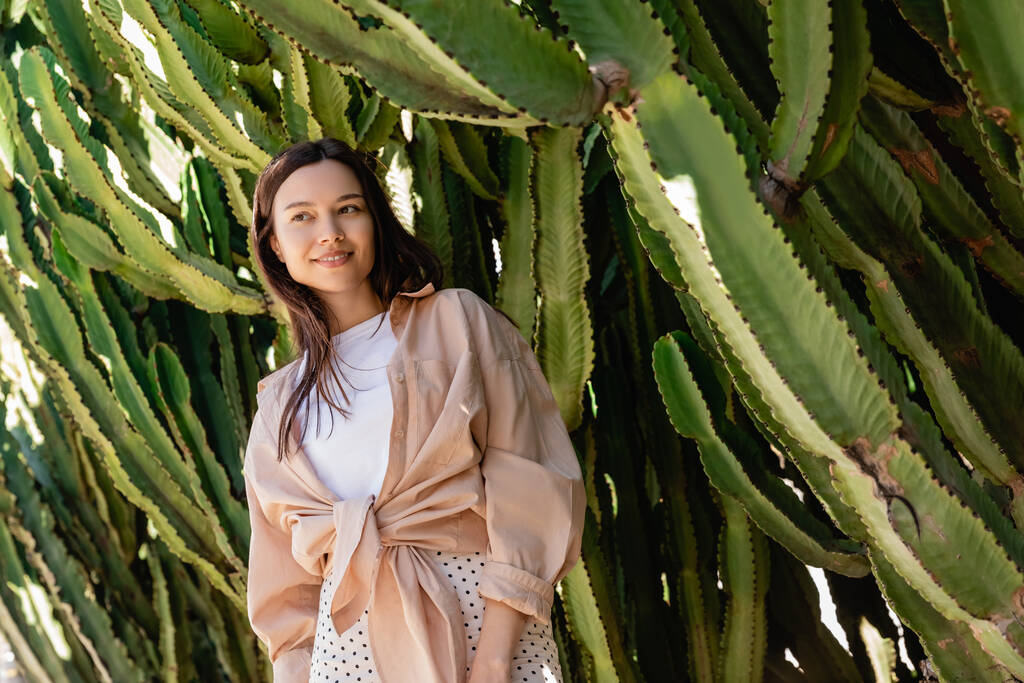 matala kulma näkymä brunette nainen paita hymyilee lähellä jättiläinen kaktukset - Valokuva, kuva