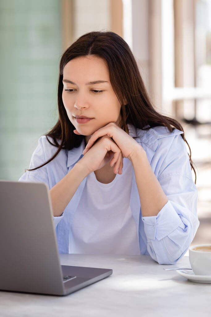 Esmer kadın kafe terasında oturuyor ve dizüstü bilgisayarına bakıyor. - Fotoğraf, Görsel