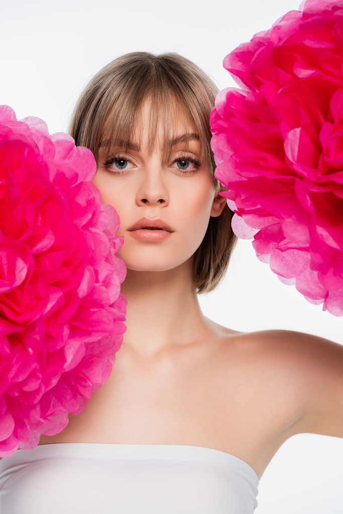 blonde young woman with bare shoulder looking at camera near bright pink flowers isolated on white - Photo, image