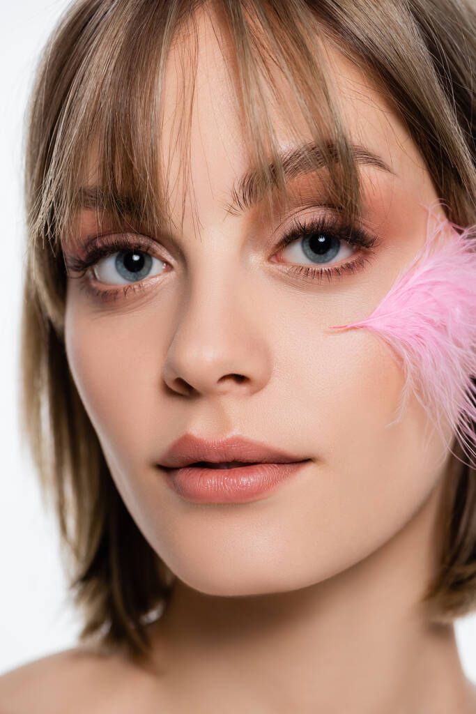 close up view of young woman with blue eyes and pink feather on face isolated on white - Photo, image