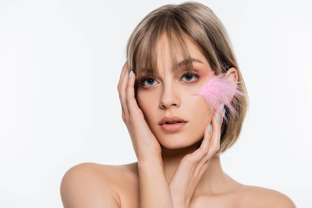 sensual young woman with blue eyes and pink feather on cheek touching face isolated on white - Foto, afbeelding