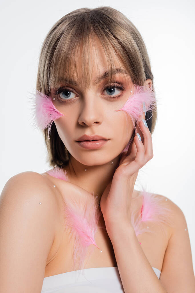 pretty young woman with decorative elements on face and body and pink feathers on cheeks isolated on white - Foto, immagini