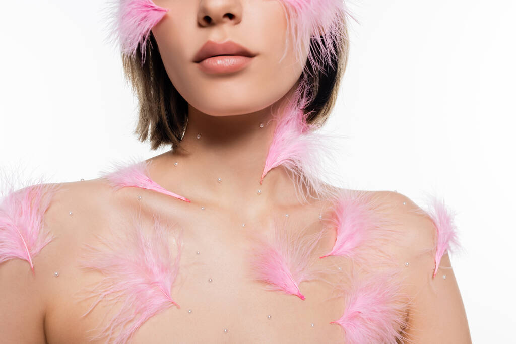обрезанный вид молодой женщины с декоративными элементами и розовыми перьями на лице и теле изолированы на белом - Фото, изображение