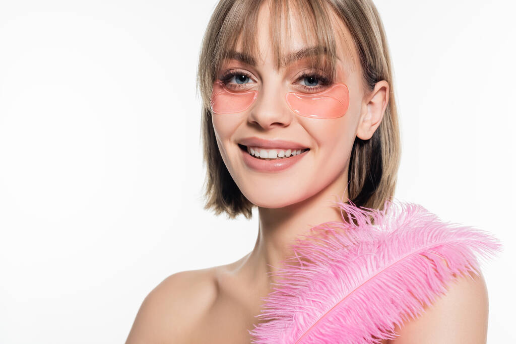 усміхнена молода жінка з гідрогелевими плямами очей тримає рожеве перо ізольовано на білому
 - Фото, зображення