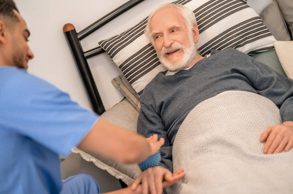 Oudere patiënt die thuis een fysiotherapiesessie ondergaat - Foto, afbeelding