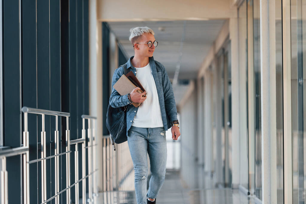 Чоловік молодий студент в джинсовому одязі в коридорі коледжу з книгами в руках
. - Фото, зображення