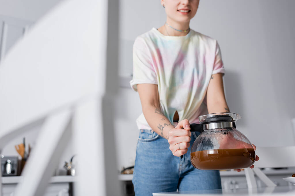 visão parcial da mulher sorridente com panela de café na cozinha em primeiro plano borrado - Foto, Imagem