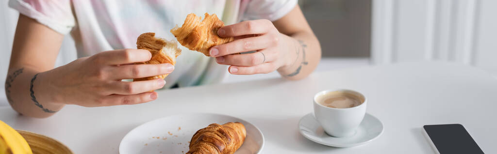 vista parcial de la mujer sosteniendo delicioso croissant cerca de la taza de café, bandera - Foto, Imagen
