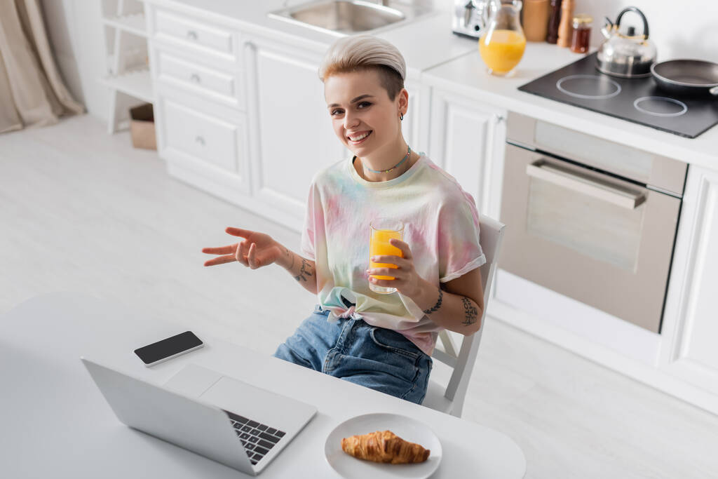 ノートパソコンやスマートフォンやクロワッサンの近くにオレンジジュースの幸せな女性の高い角度のビュー - 写真・画像