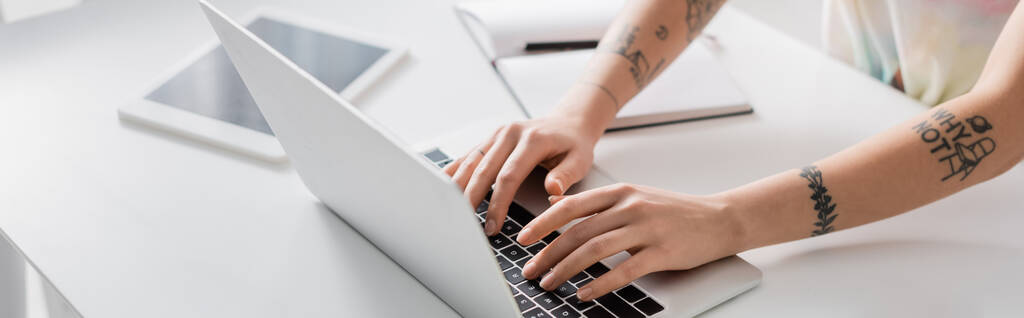 partial view of tattooed woman typing on laptop near notebook and blurred laptop, banner - Foto, Imagem