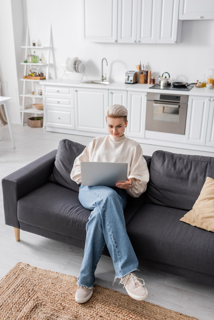 high angle view of trendy woman using laptop on sofa in modern open plan kitchen - Photo, image