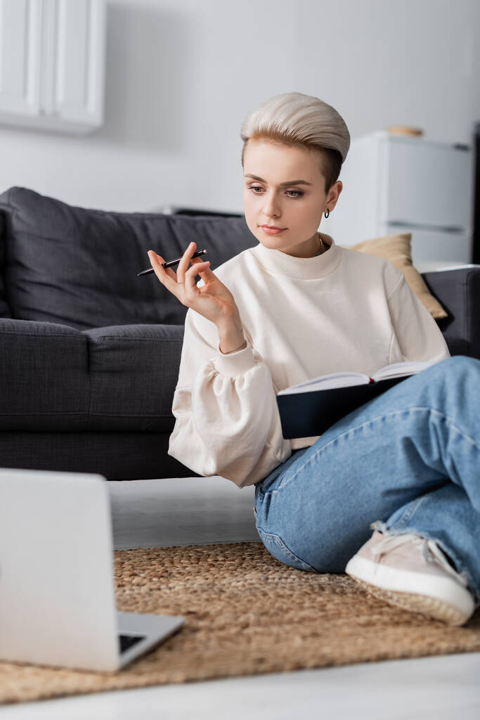 trendy woman with notebook and pen sitting on floor near laptop - Φωτογραφία, εικόνα