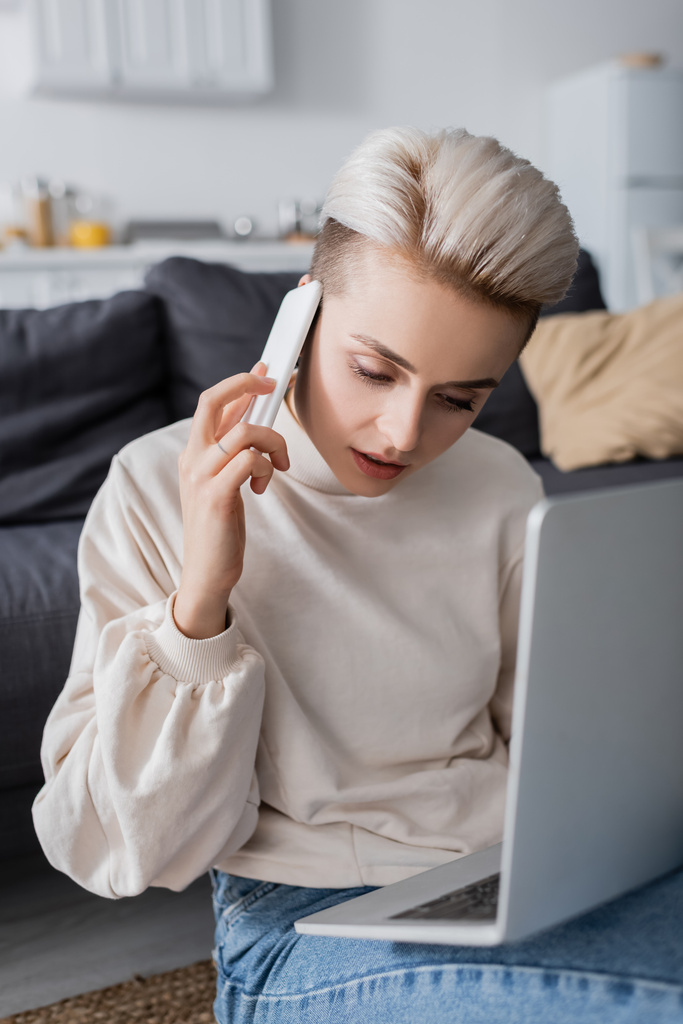 woman in white pullover calling on mobile phone near blurred laptop - Photo, image