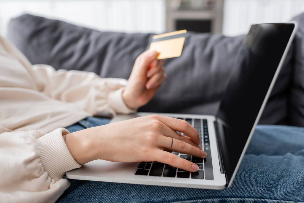 partial view of woman holding credit card and typing on laptop with blank screen - Foto, Imagen