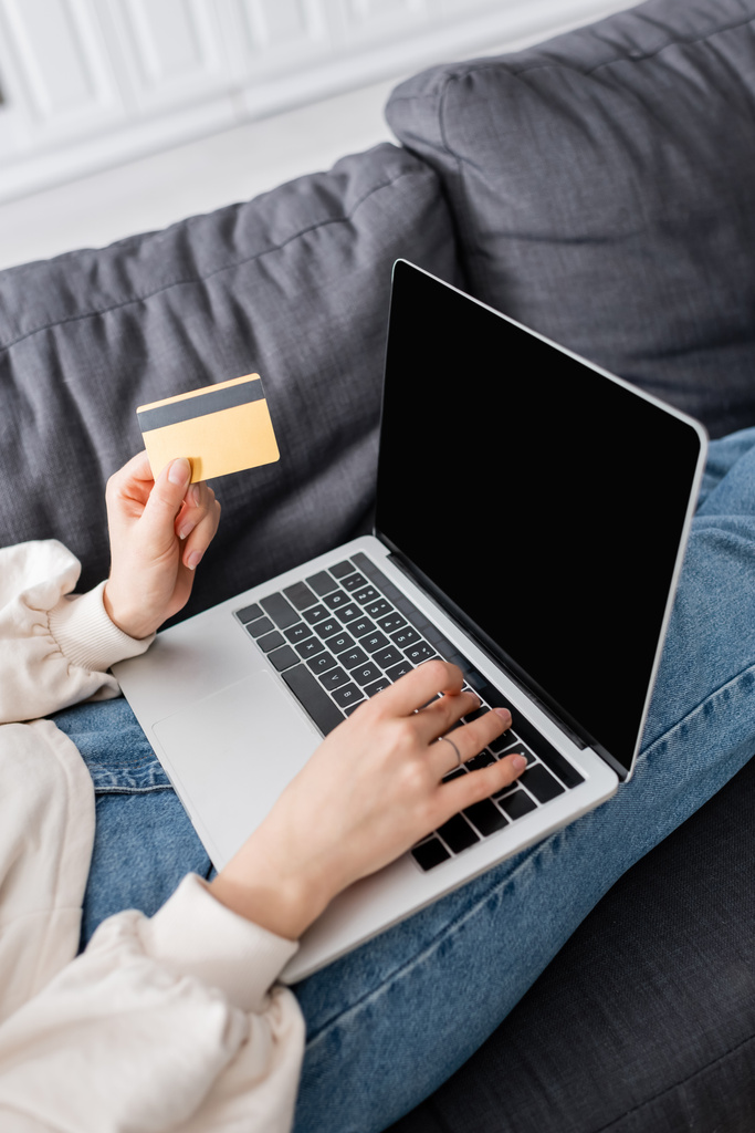bijgesneden weergave van vrouw met laptop en creditcard op bank thuis - Foto, afbeelding