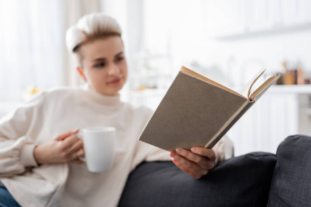 wazige vrouw met kopje thee lezen boek thuis - Foto, afbeelding