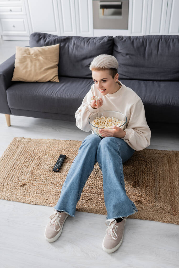high angle view of young woman eating popcorn while watching tv on floor at home - Foto, immagini