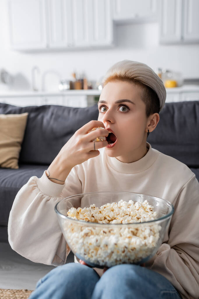 astonished woman watching tv and eating popcorn at home - Fotografie, Obrázek