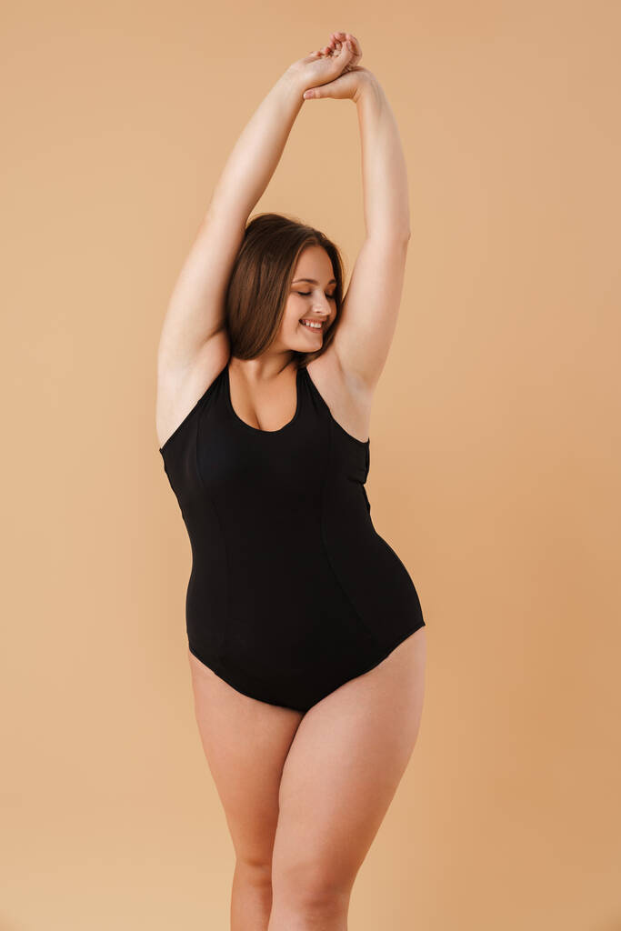 Young woman wearing swimsuit smiling while posing on camera isolated over beige background - Photo, image