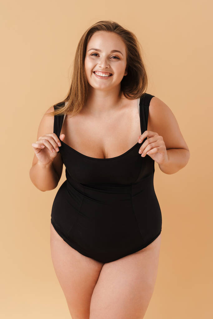 Young woman wearing swimsuit smiling and looking at camera isolated over beige background - Foto, imagen