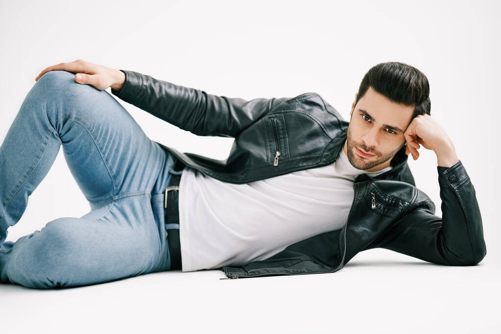 Schöner stylischer Mann posiert auf dem Boden liegend über weißem Studiohintergrund. - Foto, Bild