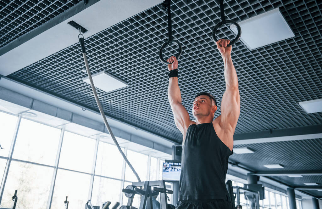 Сильний молодий чоловік у спортивному одязі робить вправи на гімнастичних кільцях у спортзалі
. - Фото, зображення
