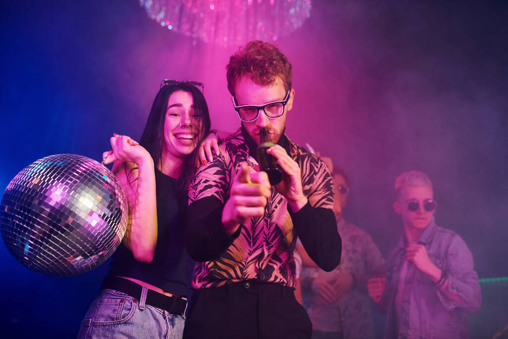 Guy in glasses drinks beer. Young people is having fun in night club with colorful laser lights. - Photo, Image