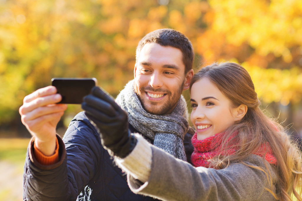 pareja sonriente con teléfono inteligente en el parque de otoño
 - Foto, imagen