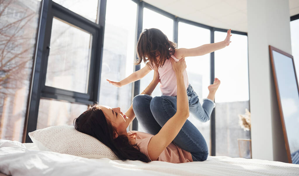 Young mother with her daughter have fun at weekend time together on bed. - 写真・画像